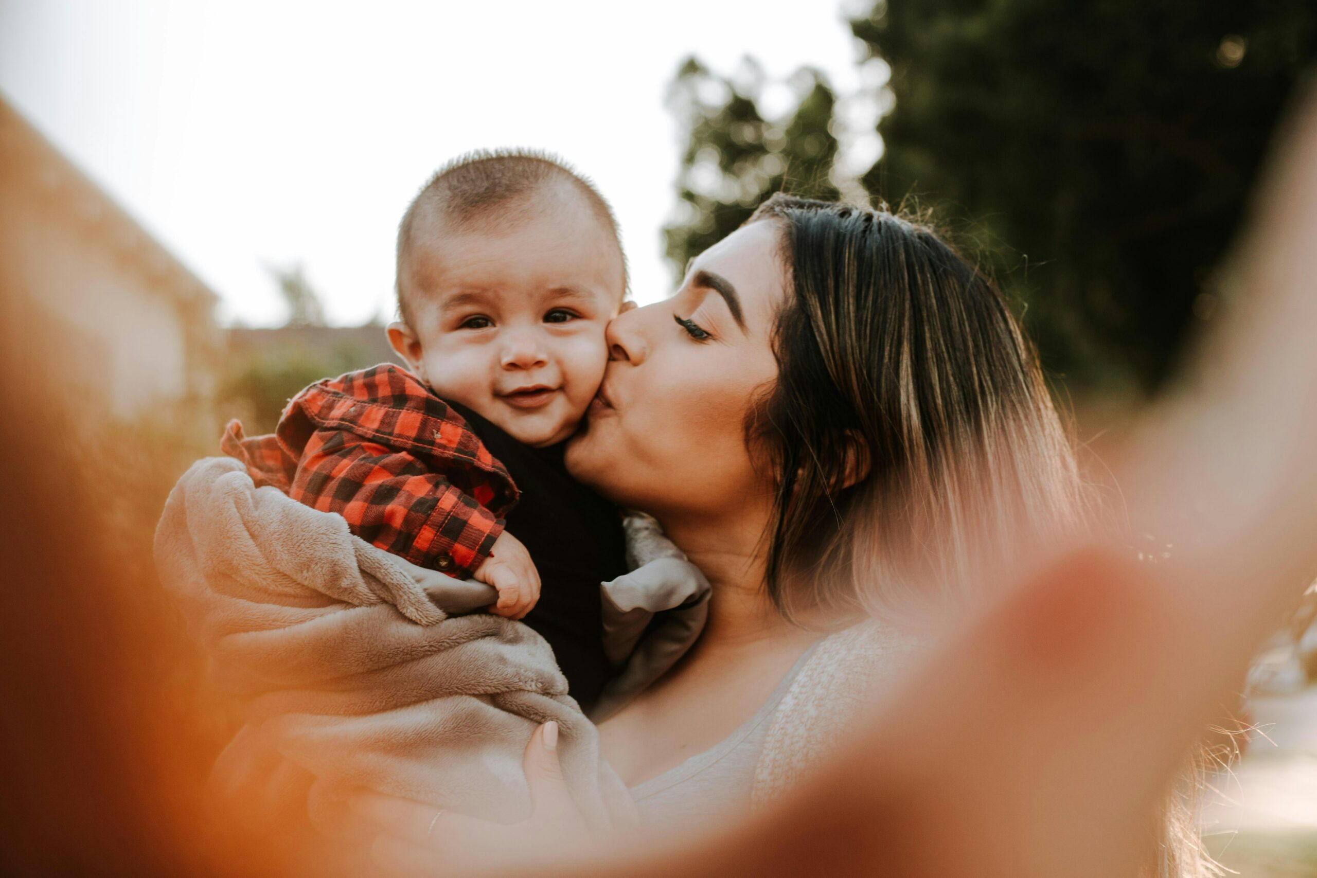 A mom holding her young child in the air and kissing his cheek.