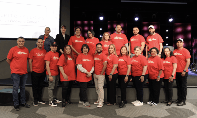 Group of people wearing red shirts, posing in two rows with a screen display behind them.